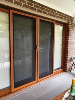 CB: 53 Double Sliding Security Doors Fitted With Stainless Steel Mesh In Cedar Wood Grain Finish & Black Trimmings Angle View.