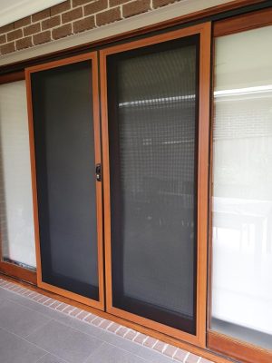 Cb: 53 Double Sliding Security Doors Fitted With Stainless Steel Mesh In Cedar Wood Grain Finish &Amp; Black Trimmings Angle View.